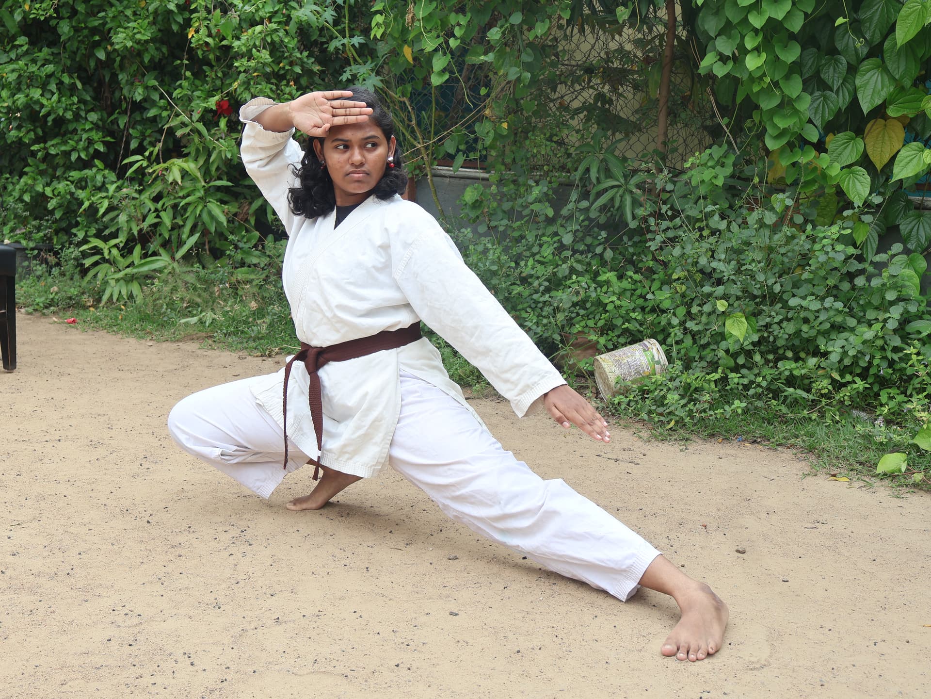 Female karate student demonstrating dynamic kata stance in traditional white gi at Tamil martial arts training center