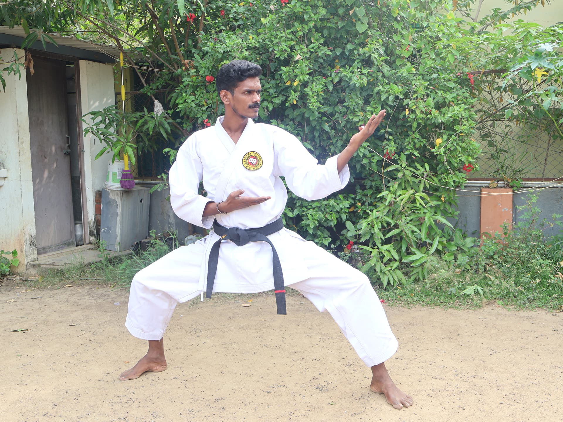 Male karate student practicing traditional kata techniques in garden training area with lush greenery